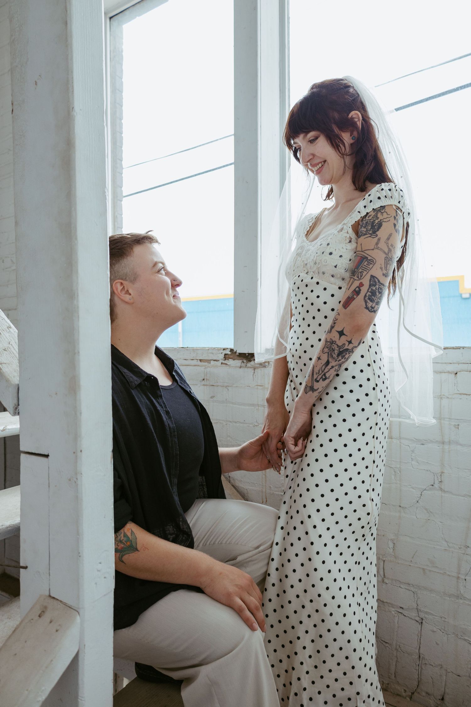 A couple sharing a tender moment by a bright window in a white-walled room.