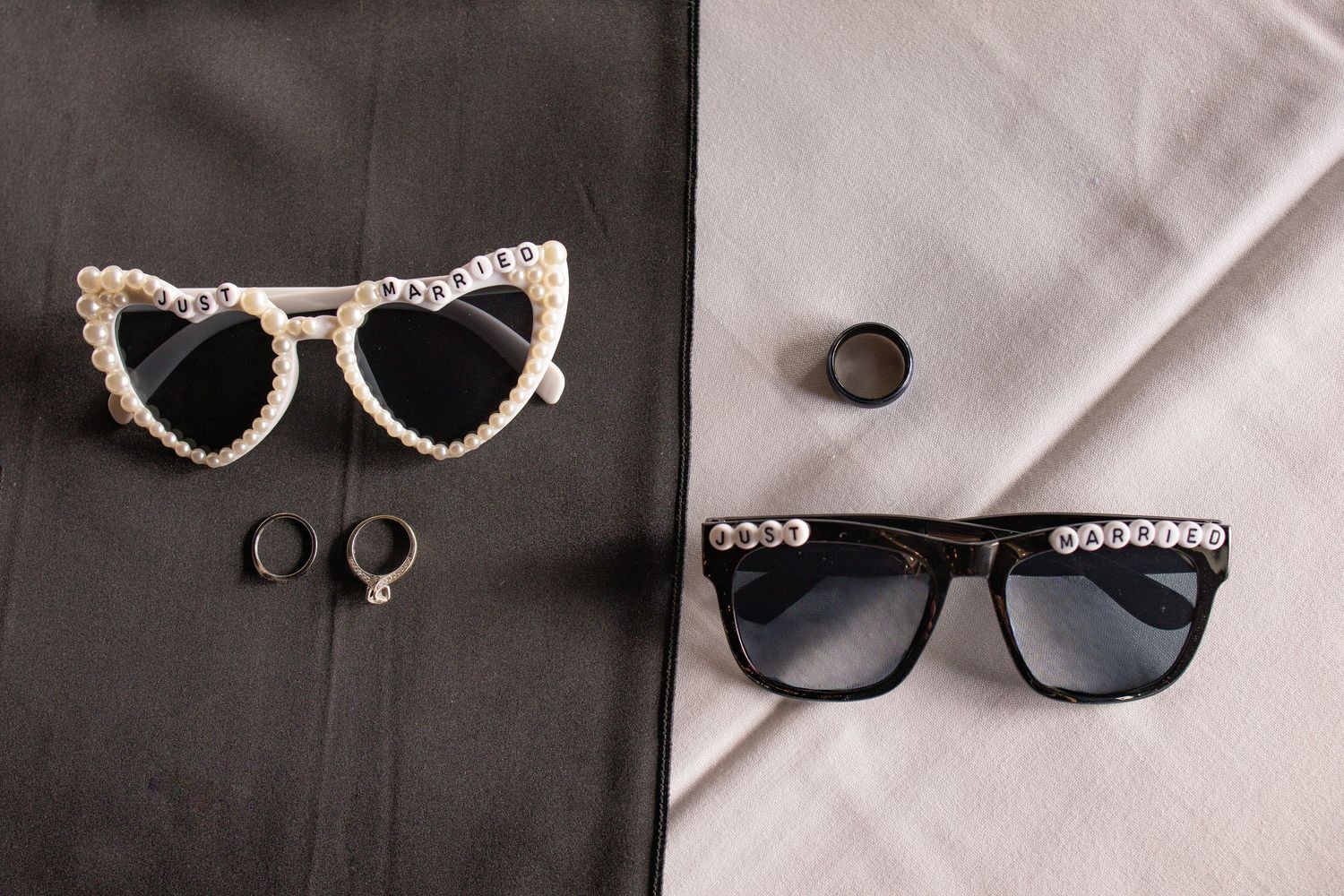 Two pairs of embellished sunglasses with pearl details and small rings arranged on black and gray fabric.