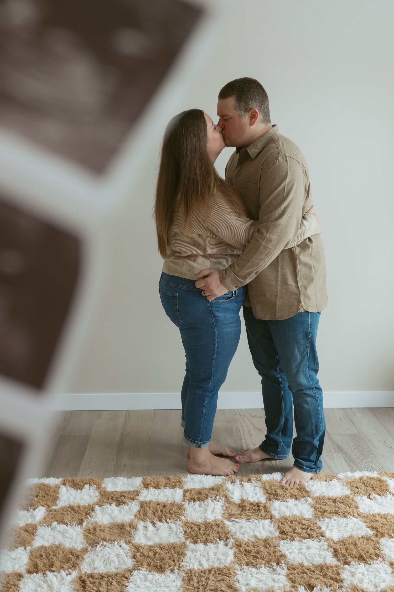 Couple kissing while holding ultrasound photos, standing on checkered rug, announcing pregnancy.
