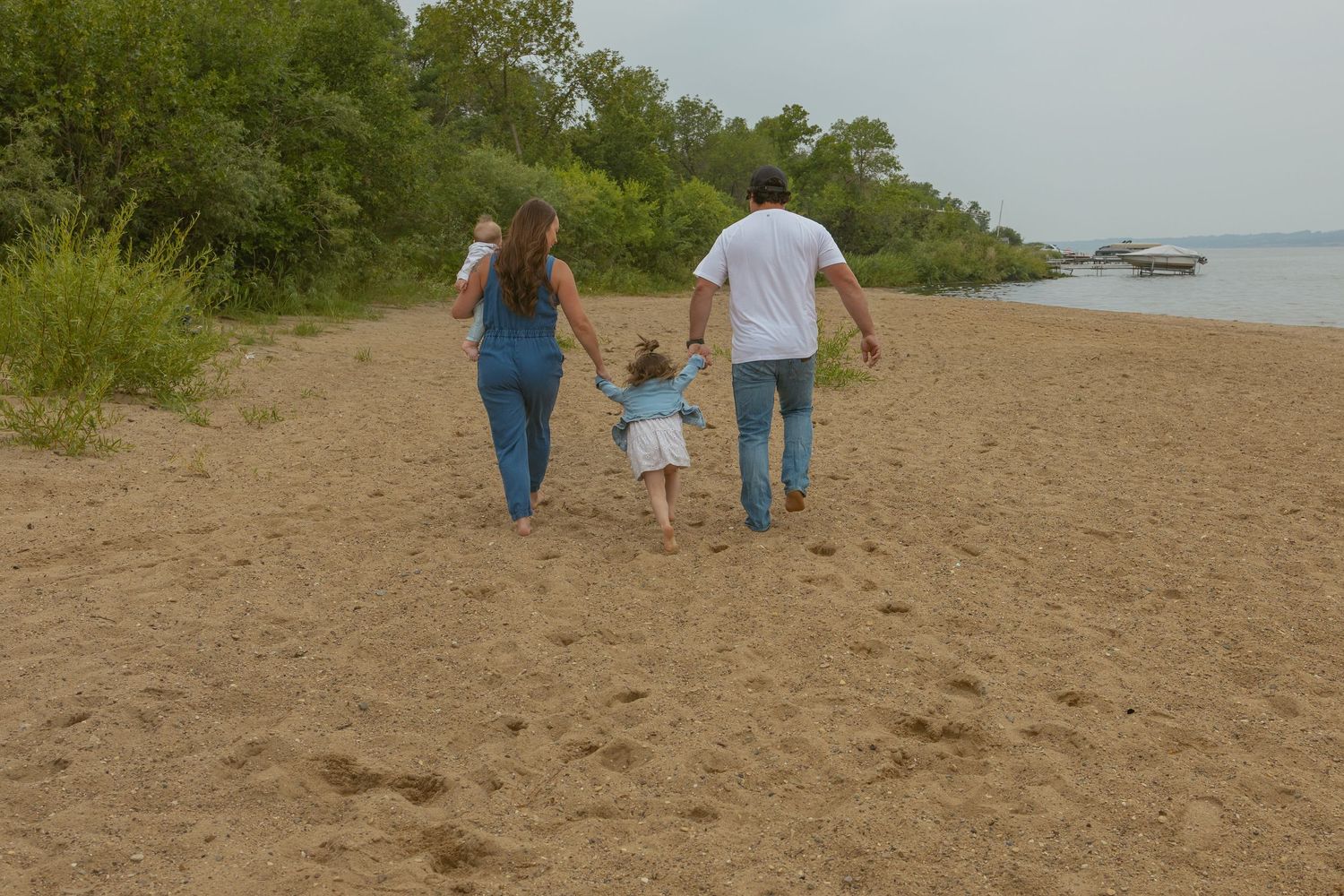 A group walks along a sandy beach path near water and vegetation.
