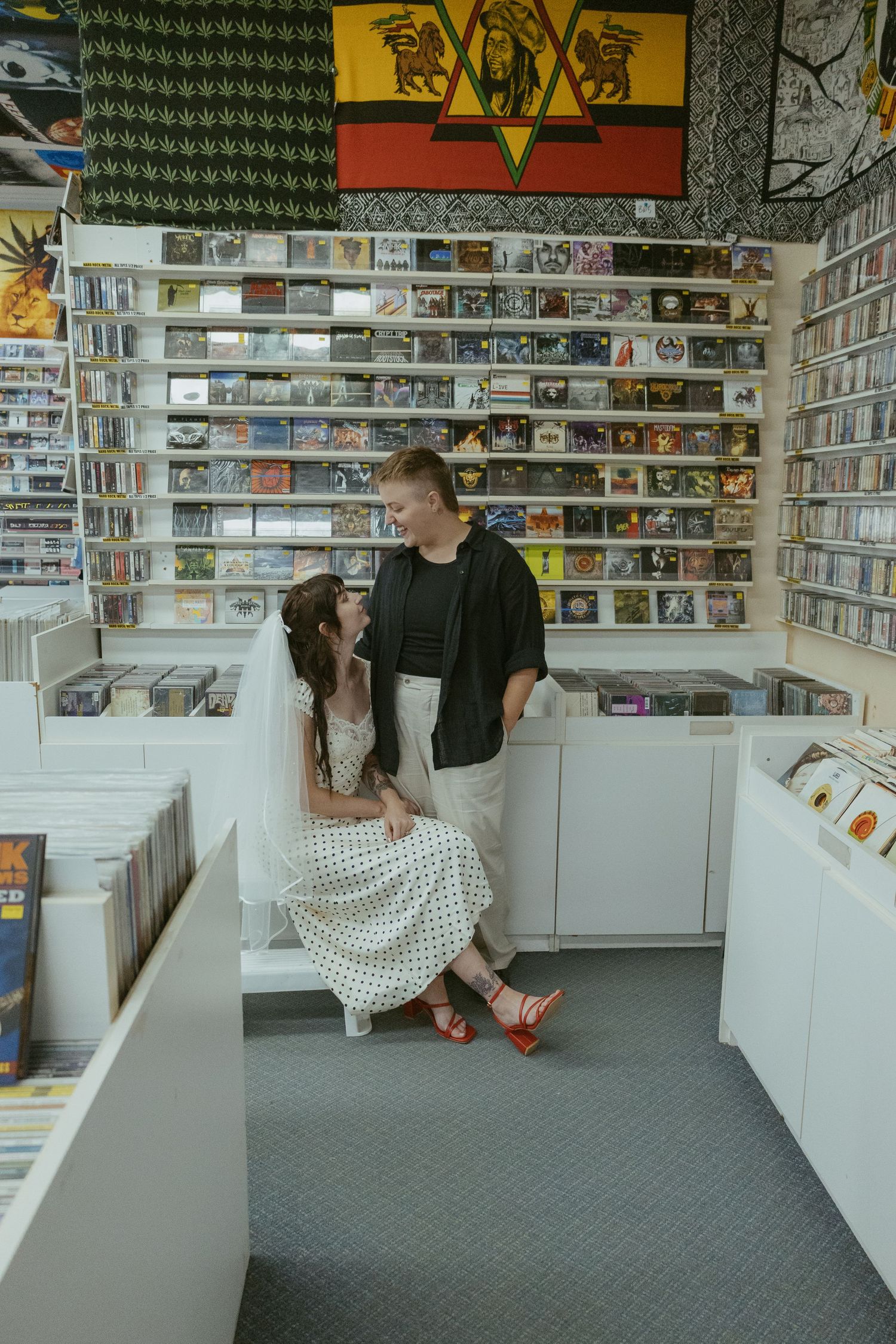 A couple poses playfully in a record store surrounded by shelves of music.