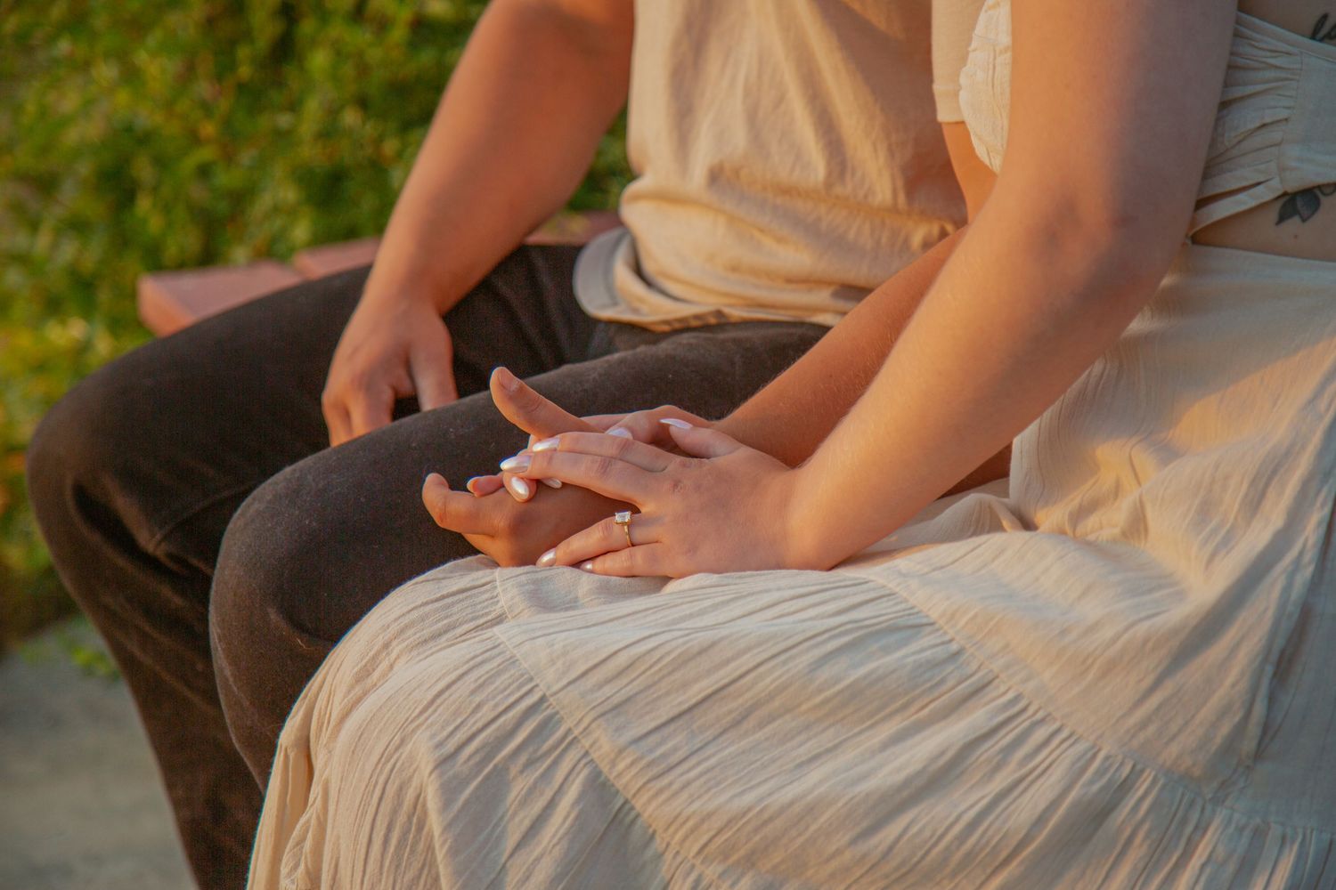 Close-up of hands resting together on a bench during sunset.
