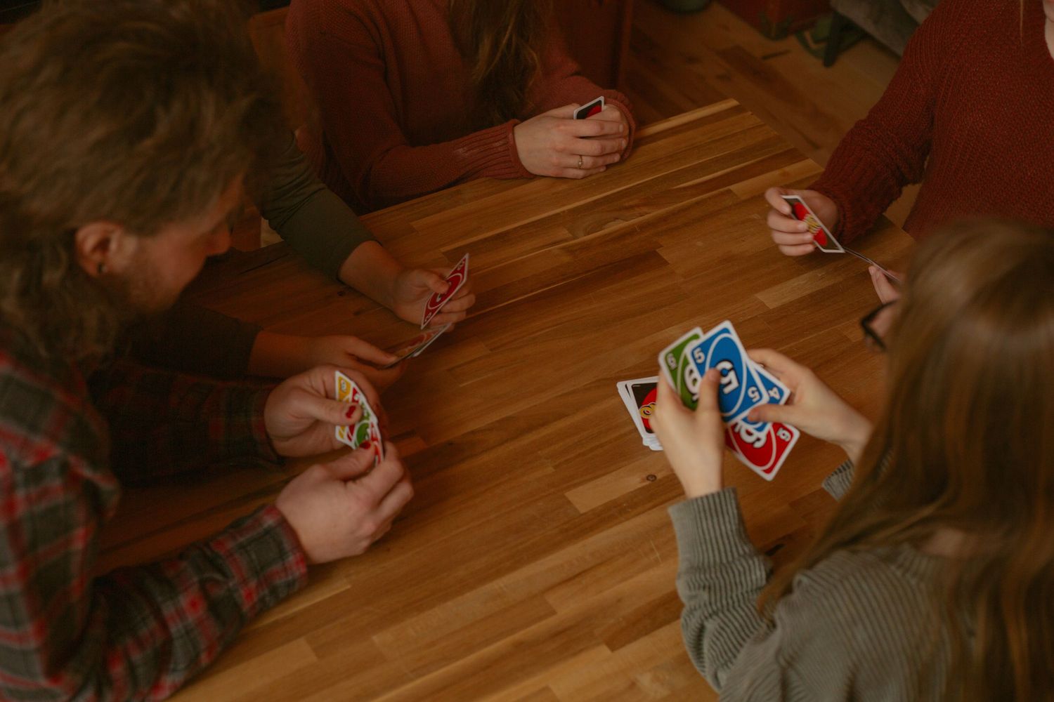 People playing card games on a wooden table in a cozy indoor setting.