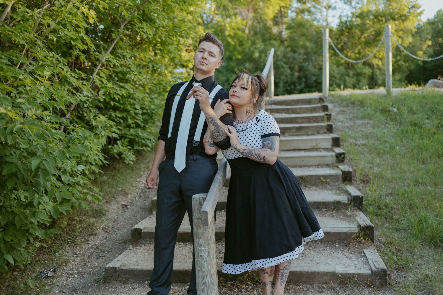 Couple in vintage formal wear posing on stone steps surrounded by greenery.