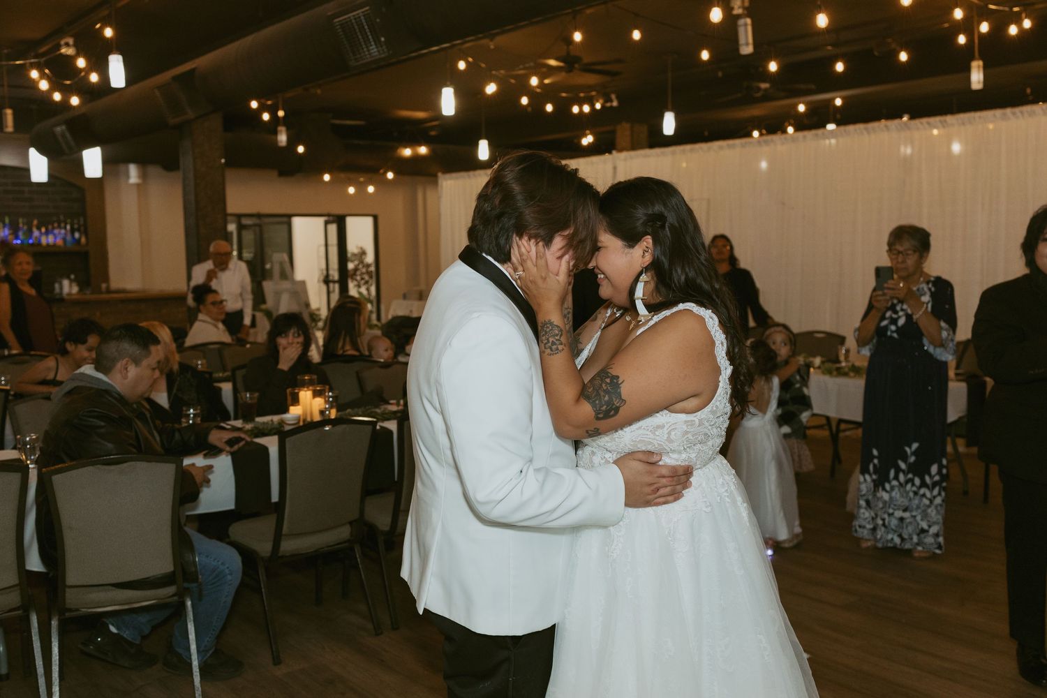 Bride and groom share their first dance at a romantic wedding reception with warm string lights.