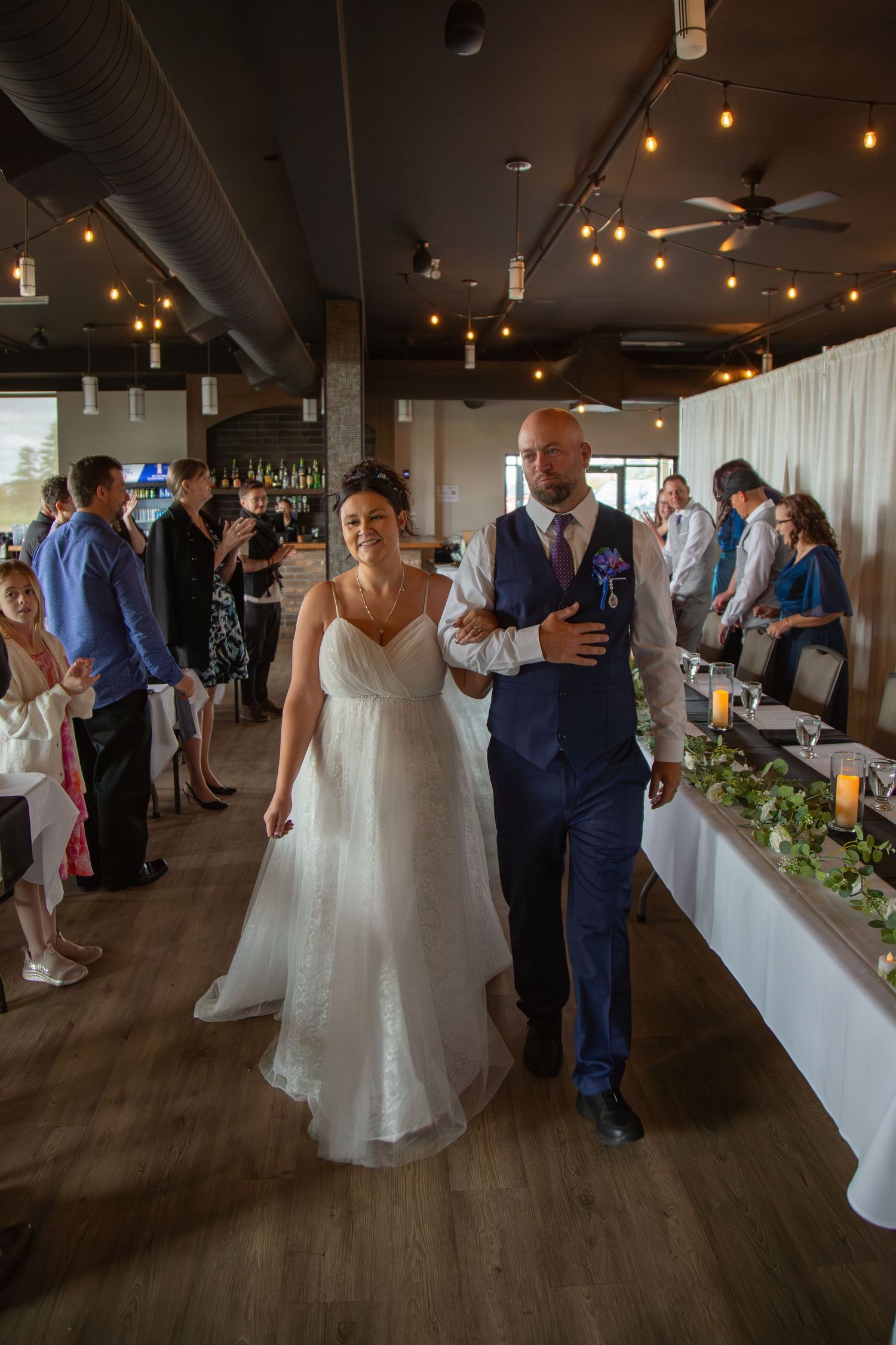 Bride in white gown and groom in navy suit walk arm-in-arm at their wedding reception venue.