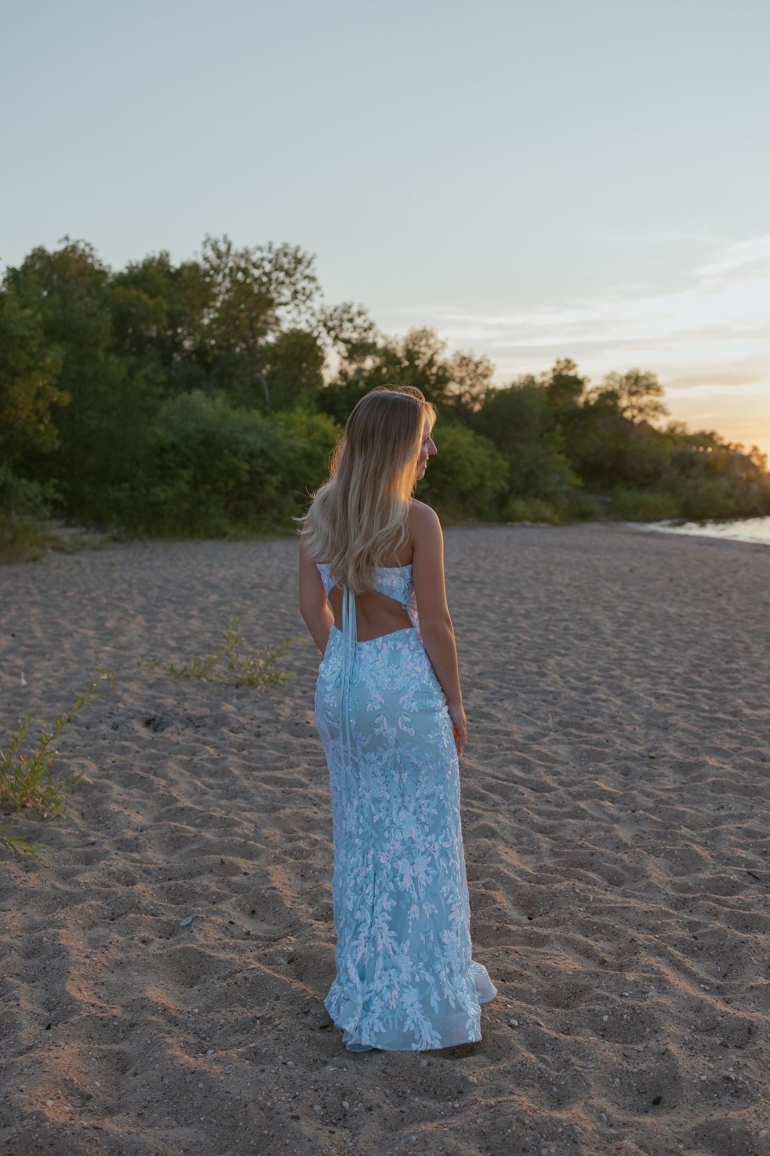 A person in a light blue dress walks along a sandy beach path during golden hour.