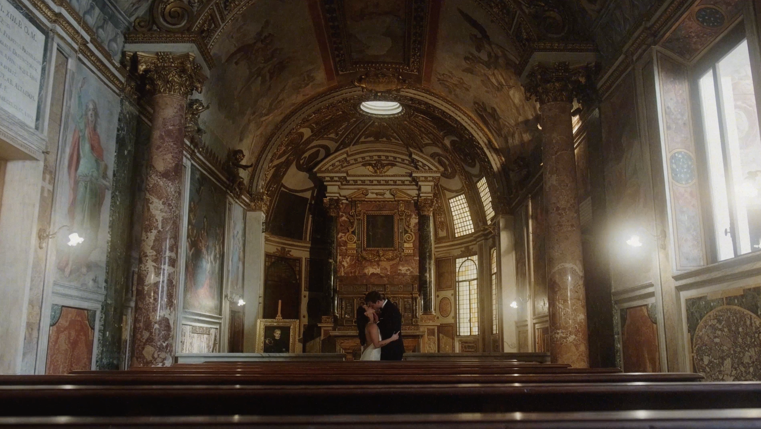 Couple sharing an intimate moment at the altar of an ornate baroque church with gilded decor and frescoed walls.