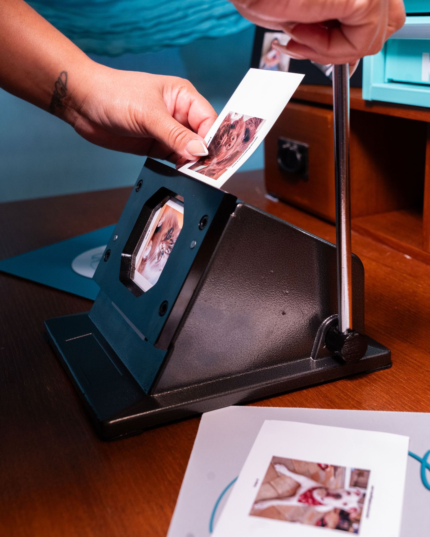 Hands placing a photo print into a black desktop photo viewer stand on a wooden desk.