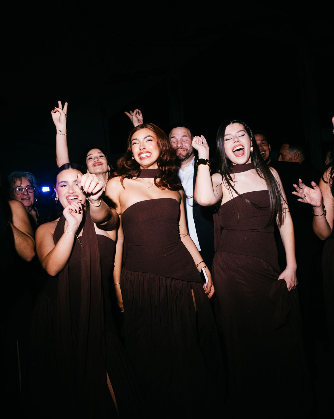 Group of women in matching brown dresses dancing and celebrating at a formal evening event.