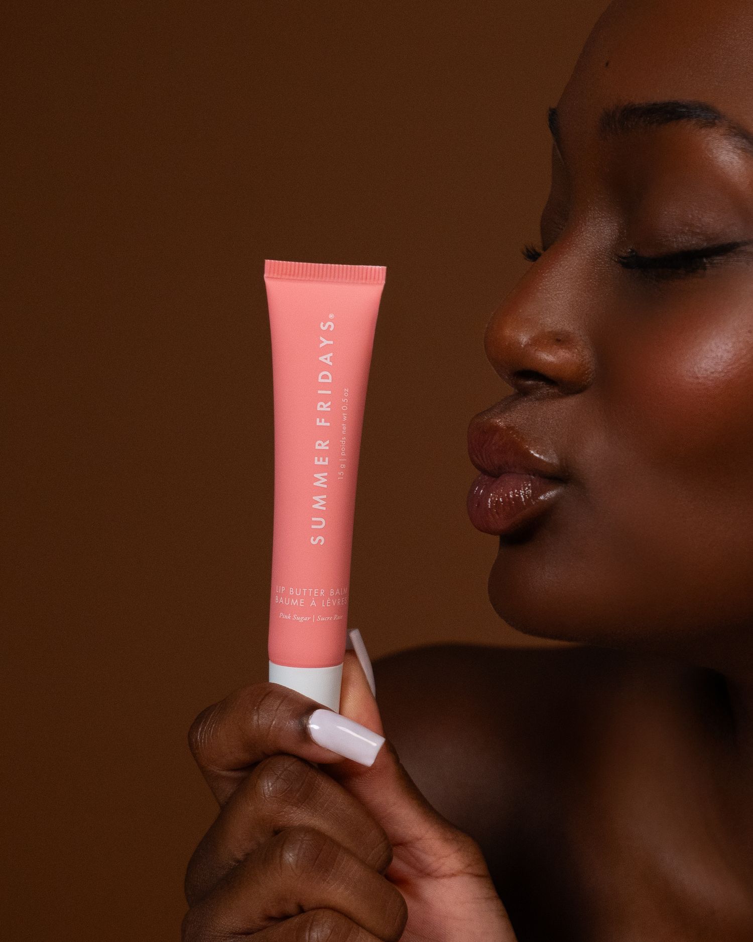 Beauty product application demonstrated on dark skin with coral-colored cosmetic tube.