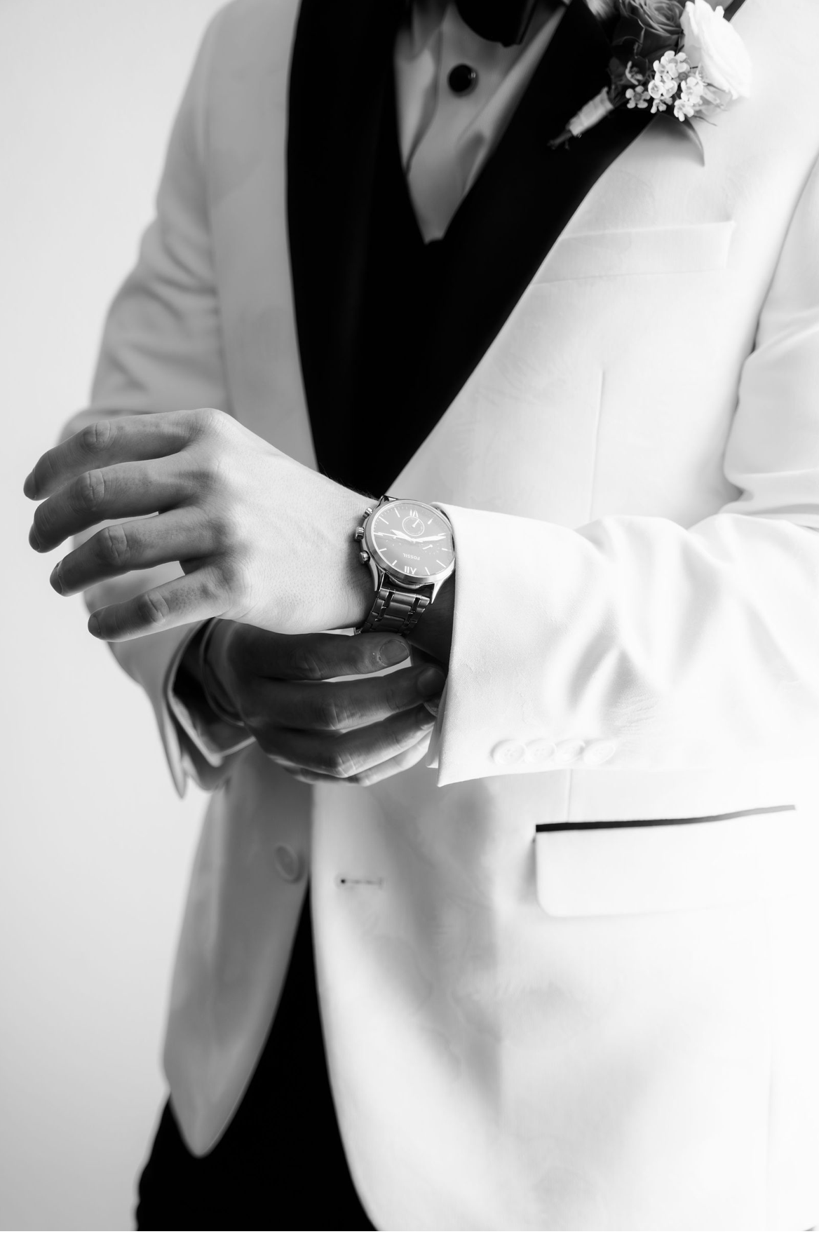 Groom in white tuxedo jacket adjusting his watch, with boutonniere, black and white photo.