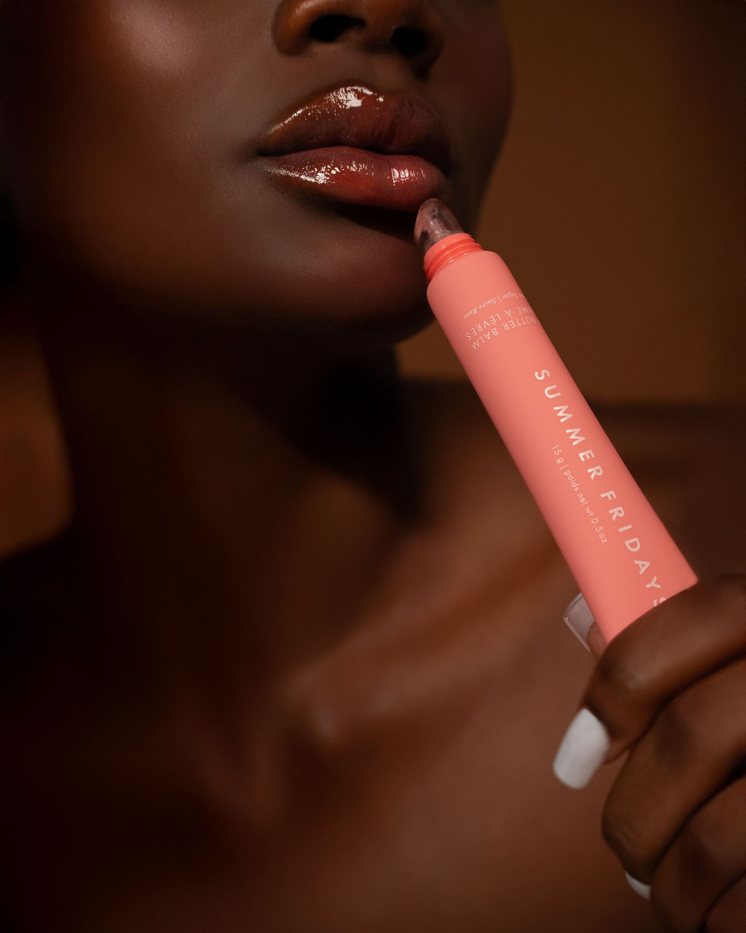 Close-up shot of glossy lips applying coral pink lipstick against a dark brown background.
