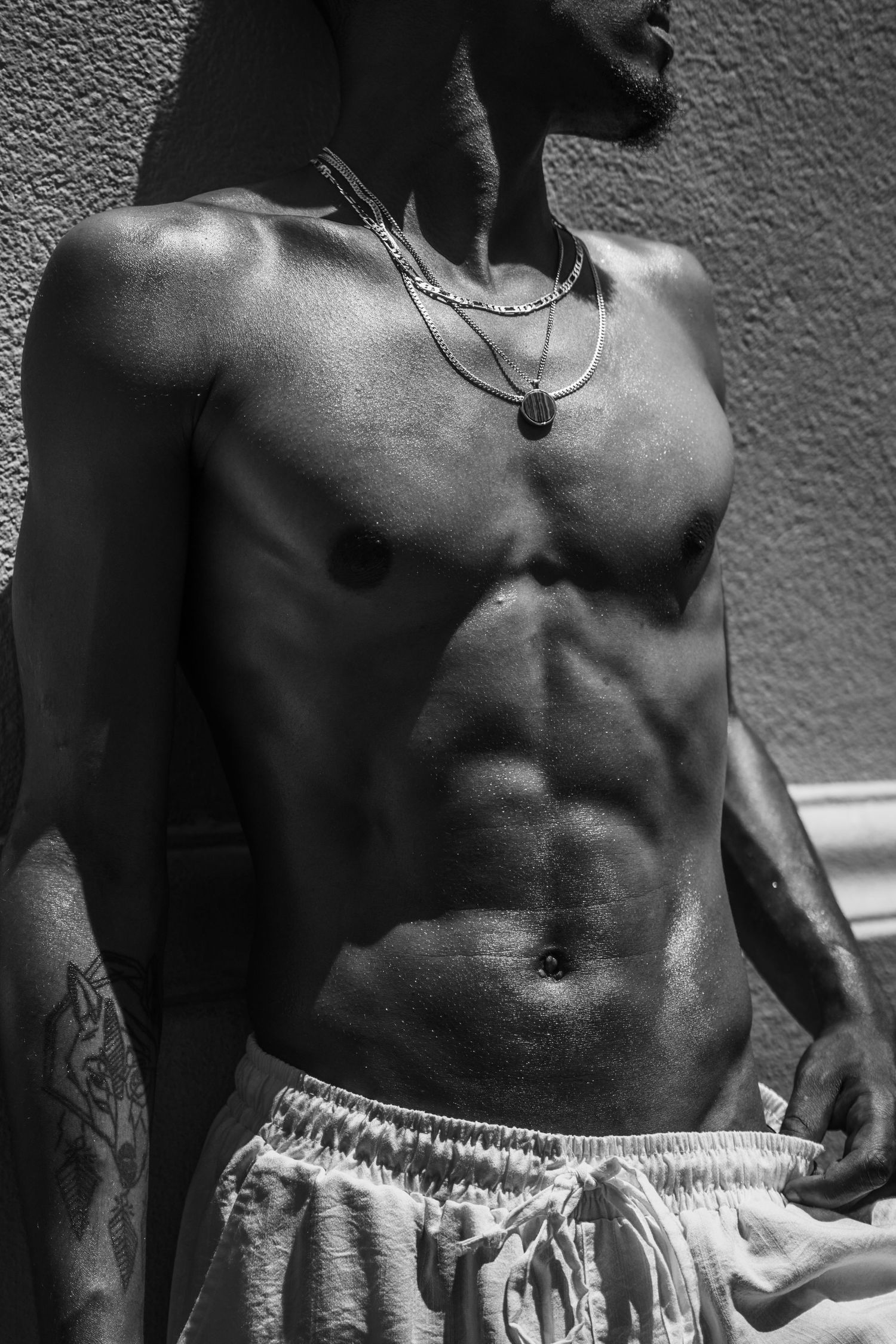 Close-up black and white photo showing muscular torso wearing white shorts against textured wall background.
