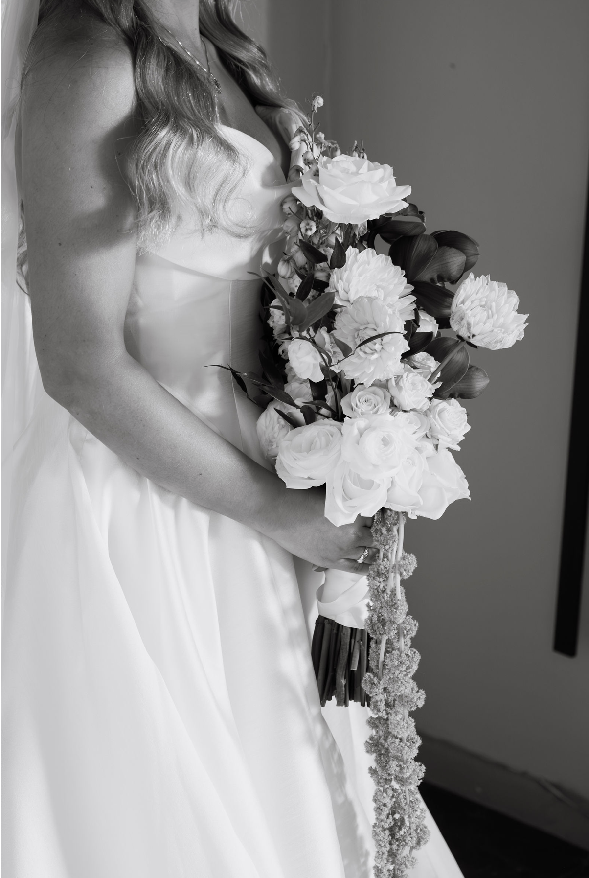 Black and white photo of a bride in a white gown holding a lush bouquet of roses and flowers on her wedding day.