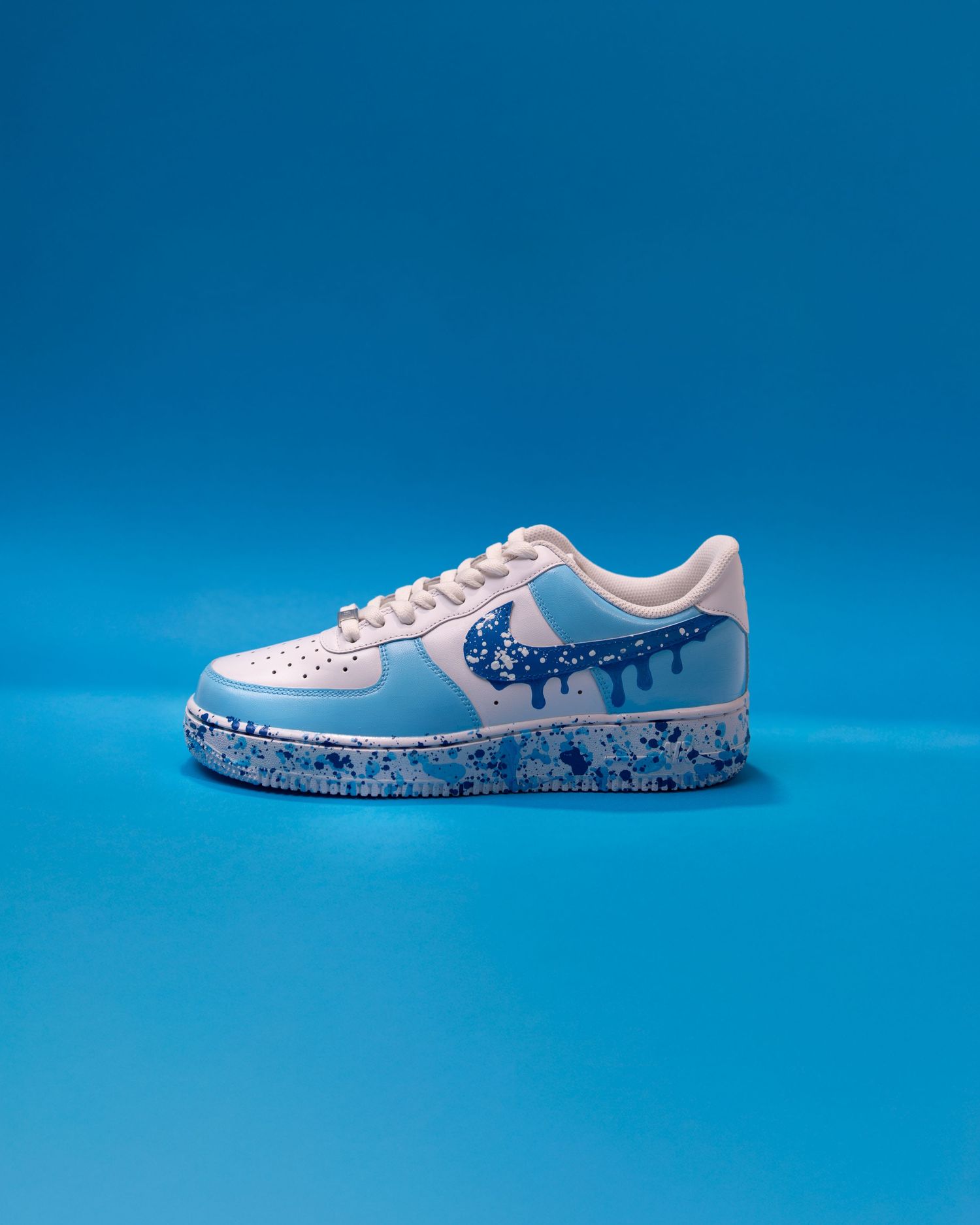 Custom Nike Air Force 1 sneaker with blue drip design, paint splatter sole, on blue background.