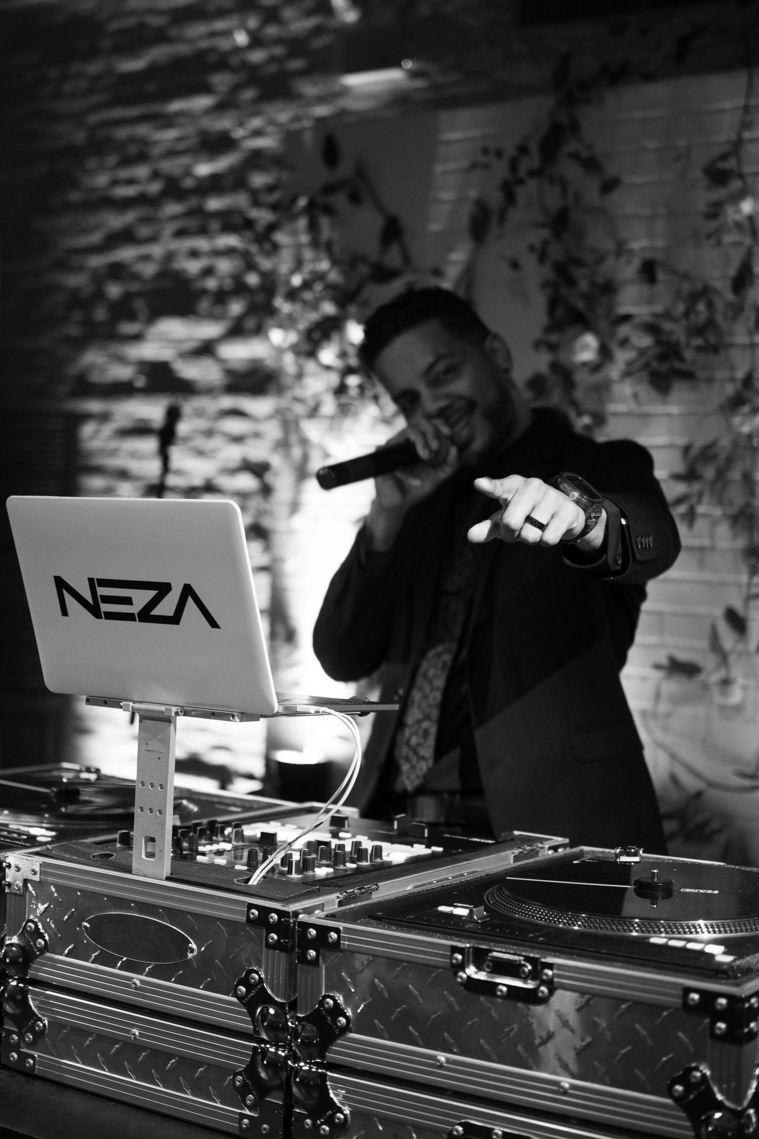 DJ performing with Neza branded equipment in dramatic black and white lighting.