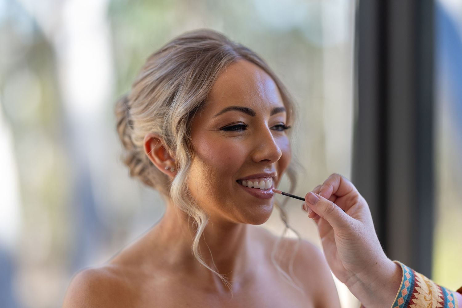 Bride smiling while getting makeup applied by a makeup artist during wedding preparations at Maya Sanctuary.