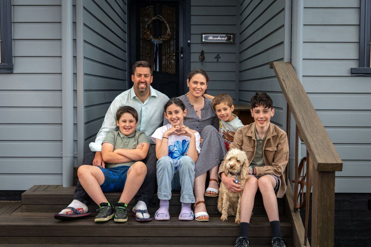 A family with children and a dog poses together on grey house front steps in Lawson, Blue Mountains.