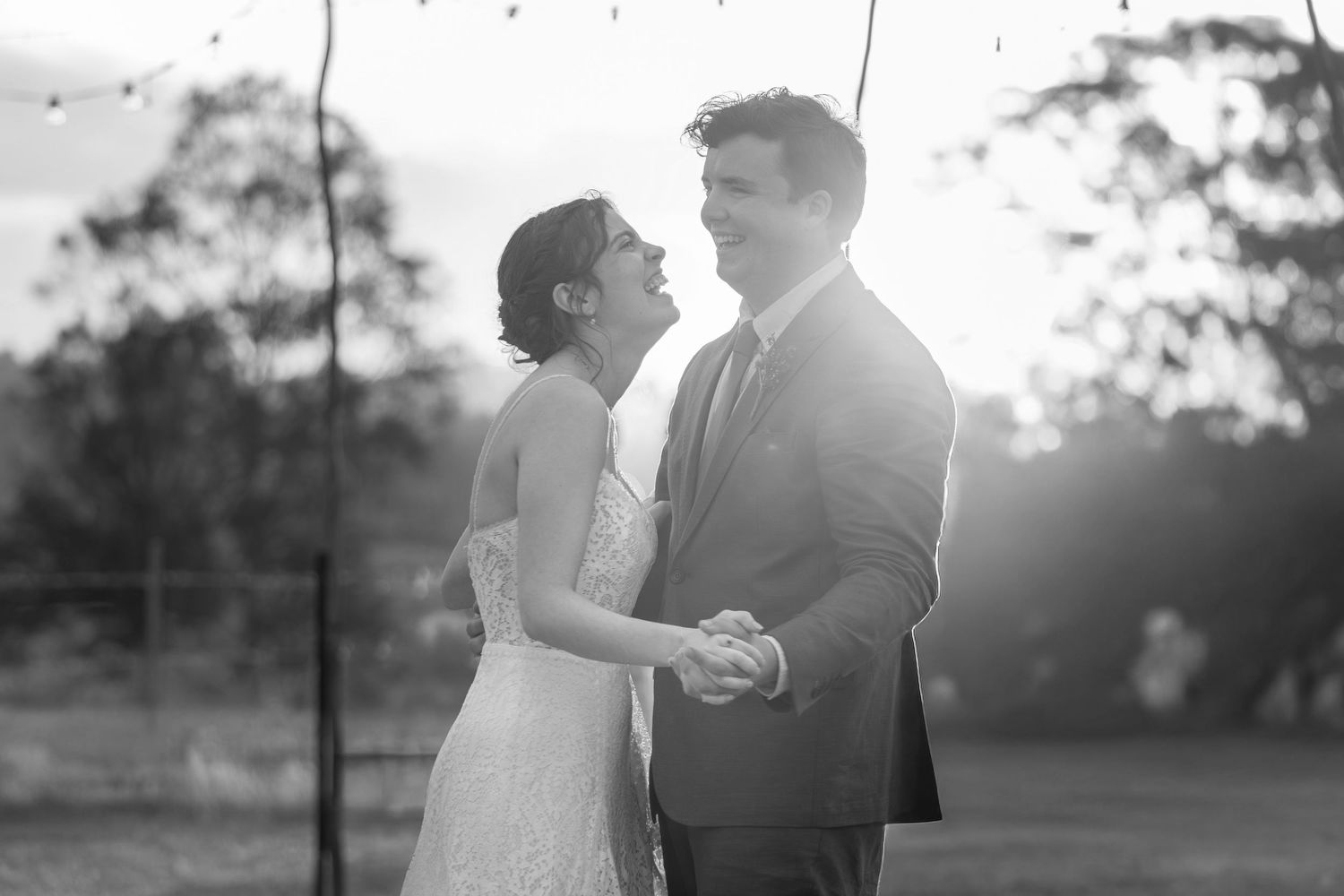 A couple in wedding attire dances together during sunset in a romantic outdoor setting.