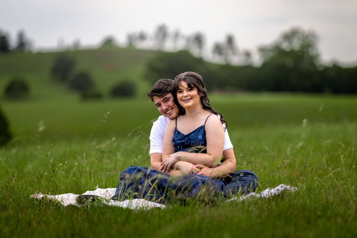 Family relaxes together on a blanket in a peaceful meadow setting.
