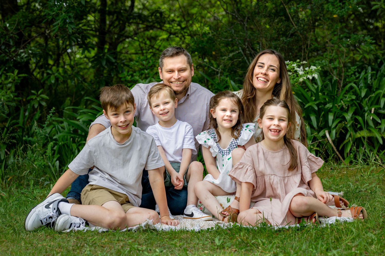 Family lying on grass during an outdoor photo session in a natural green setting.