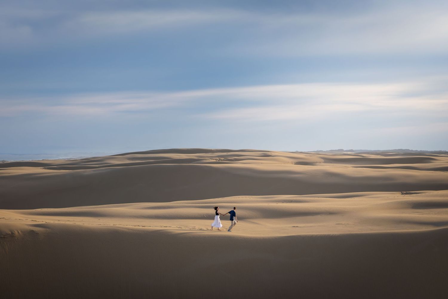 Two people running on vast golden sand dunes under a blue sky at Stockton Sand Dunes, NSW.