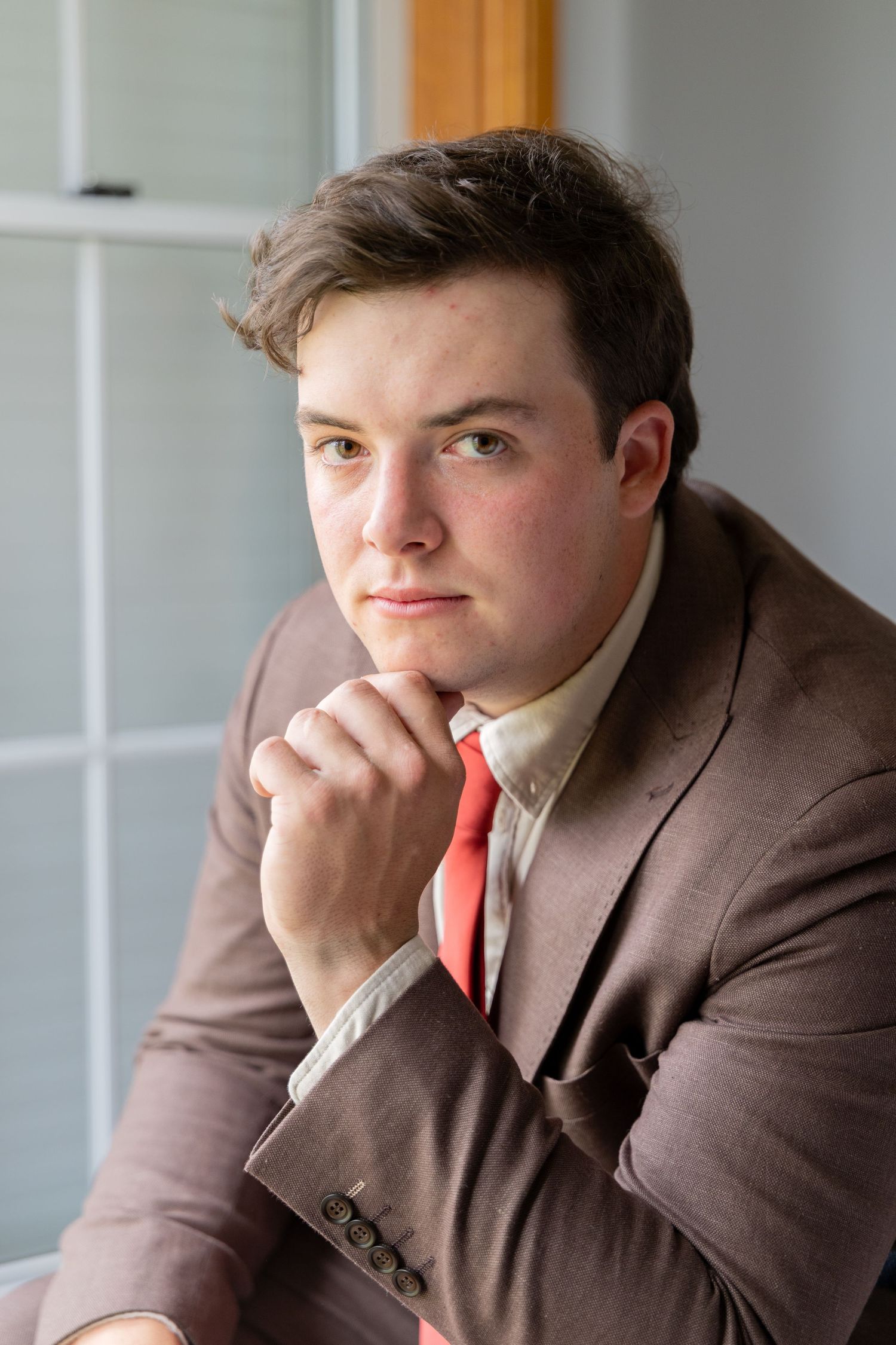 Portrait series of a person in a brown suit and red tie sitting thoughtfully by a window in Singleton, Hunter Valley.