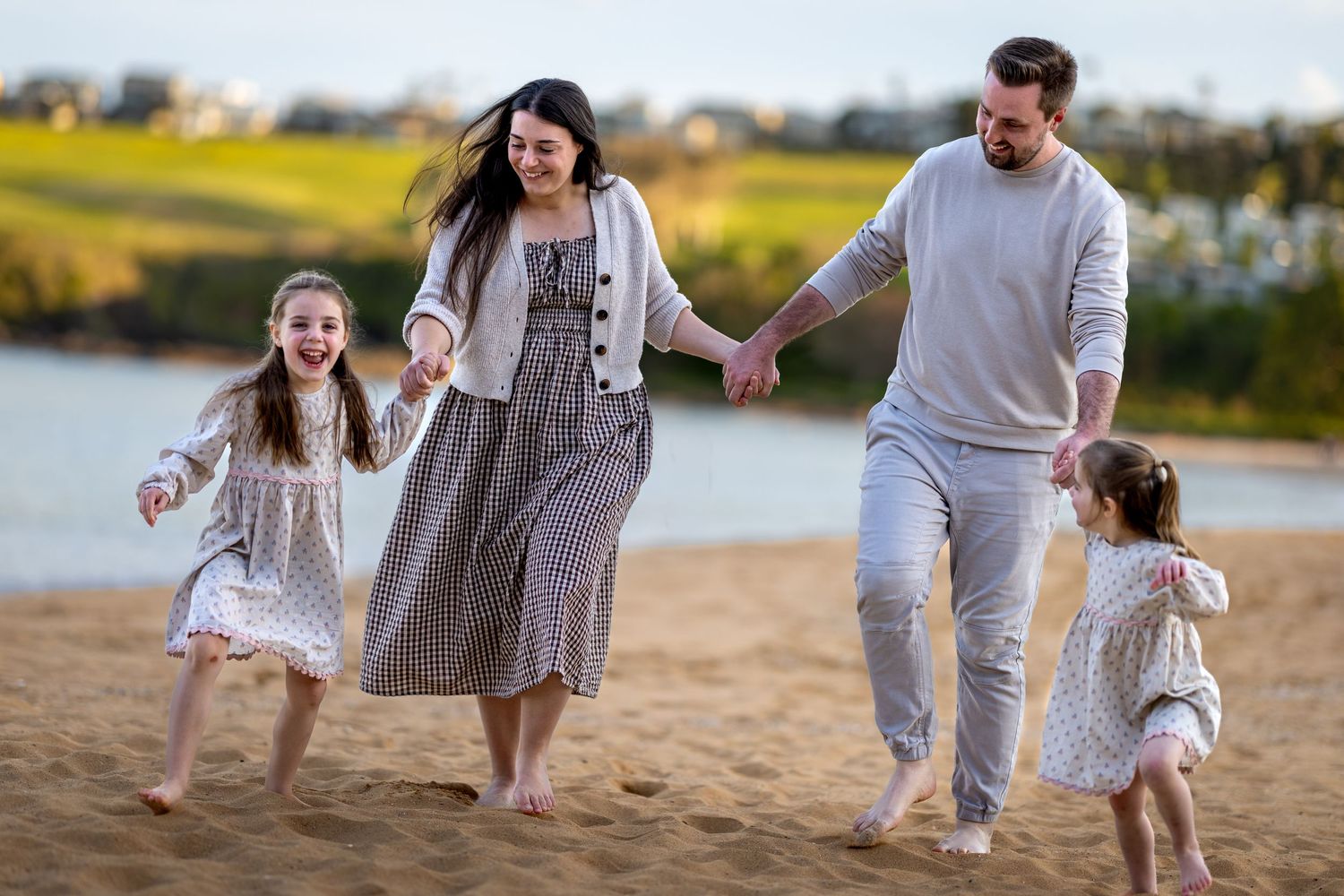 Family photo of members in white clothing chase each other joyfully across a beach during golden hour at Easts Beach, Kiama.