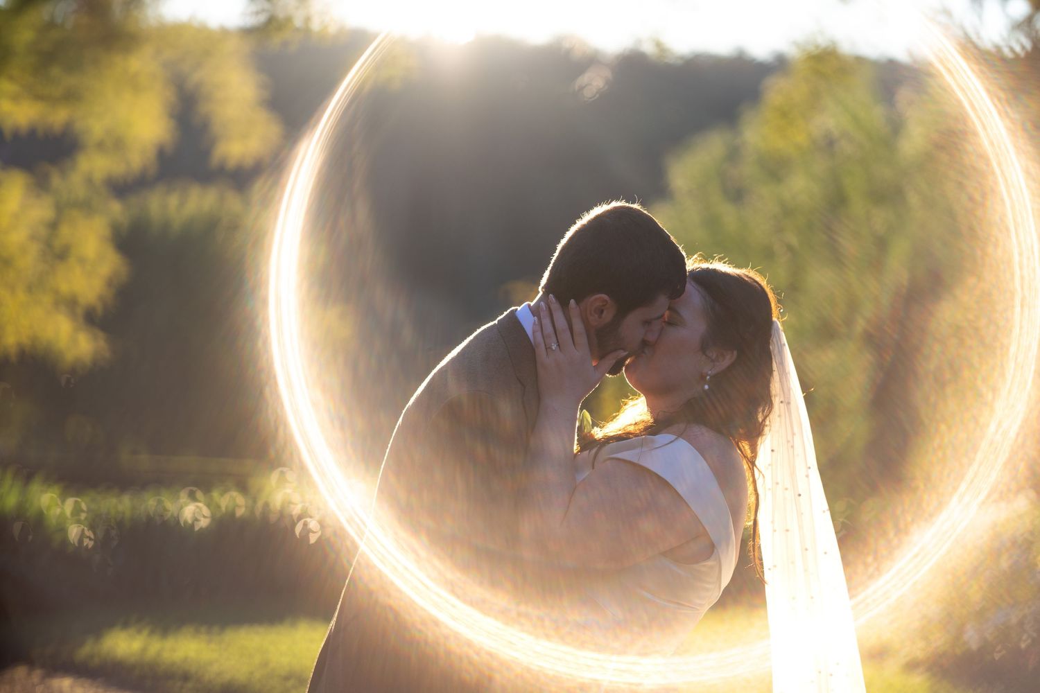 Bride and groom share a romantic kiss surrounded by a glowing circular light bokeh effect outdoors at Glenleigh Estate.