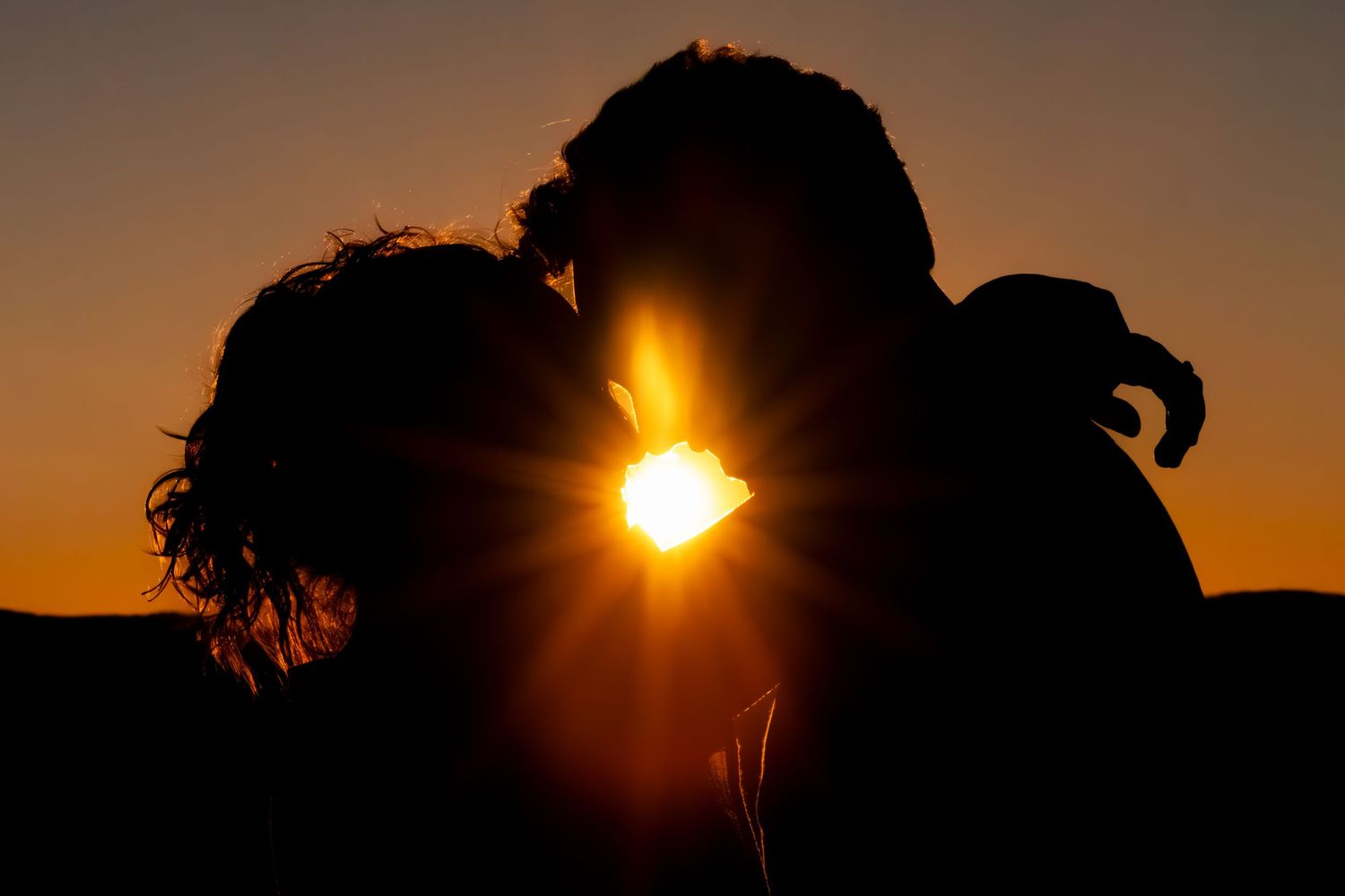 Silhouettes of a couple against dramatic sunset sky creating romantic atmosphere.