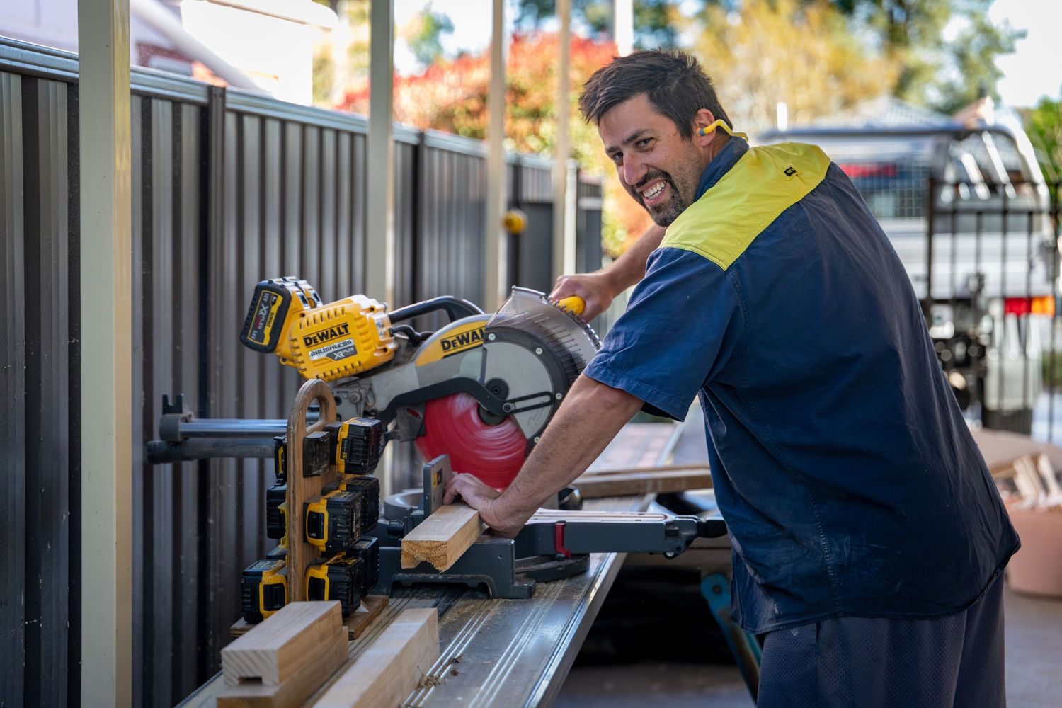 A tradie operates a drop saw while working on a metal fence installation project outdoors in Springwood, Blue Mountains.