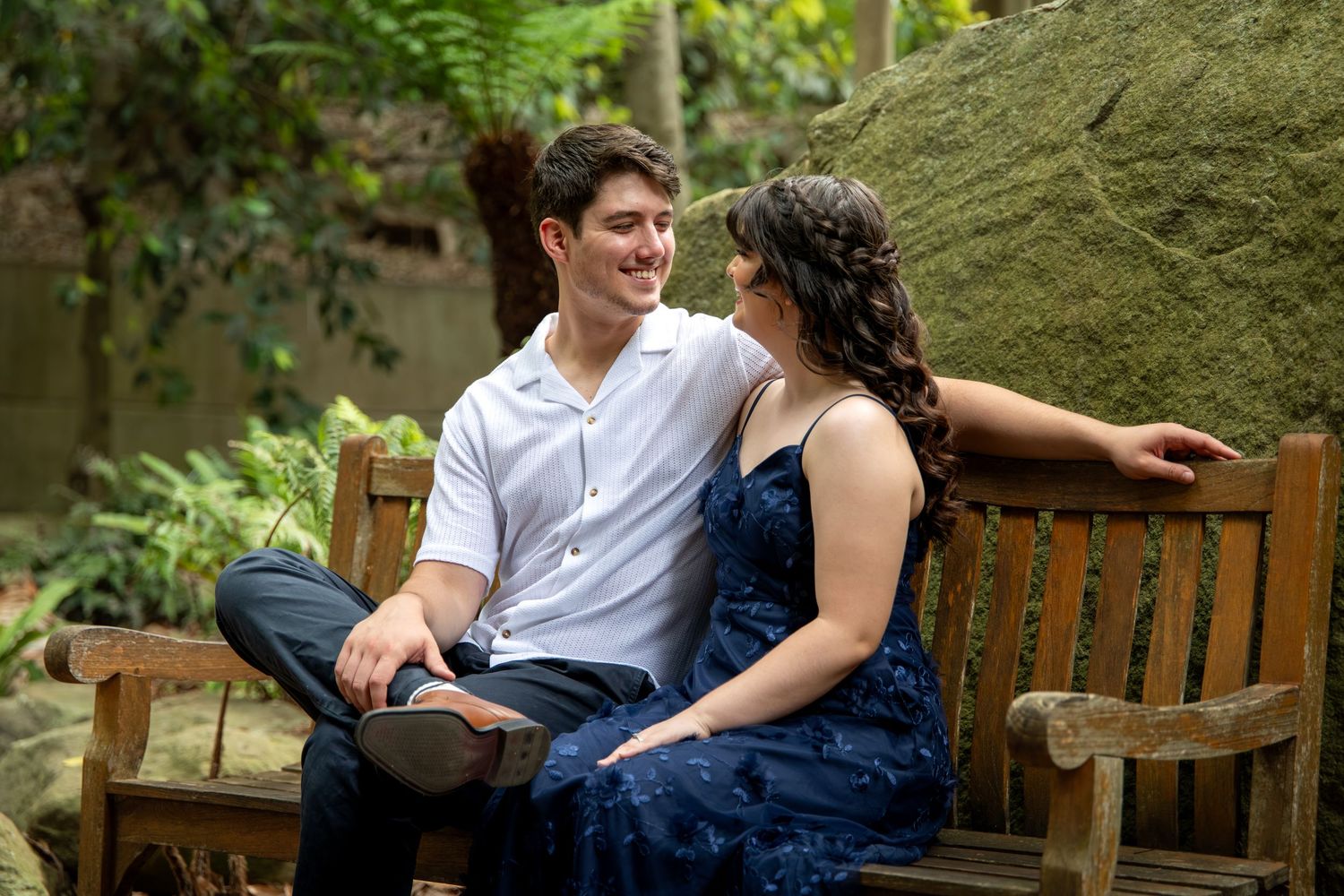 Couple sits casually together on rustic wooden bench surrounded by lush foliage at Mount Annan Botanical Gardens.