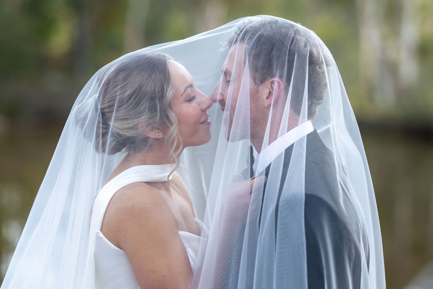 Bride and groom sharing a romantic kiss under a flowing white wedding veil outdoors at Lawson Park, Maya Sanctuary.