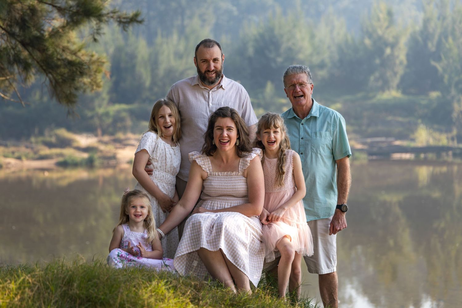 Family portrait of six people smiling Yarramundi Reserve surrounded by pine trees on a sunny day.
