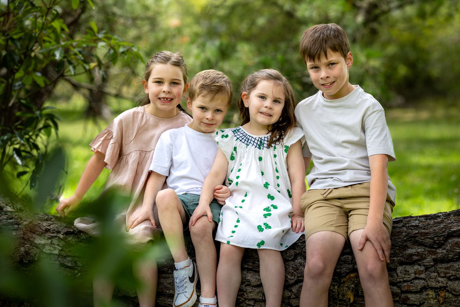 Children sitting together on rustic log during outdoor family photo session at Woodford Reserve in the Blue Mountains.