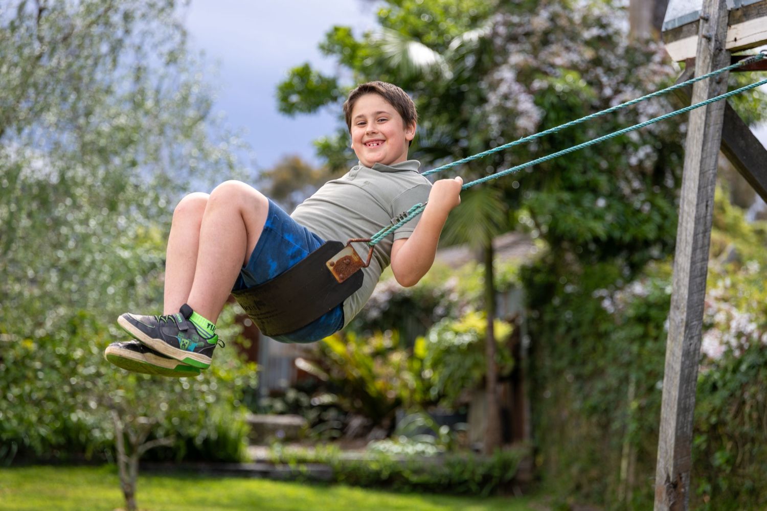 Child swinging joyfully on rope swing in sunny backyard at Lawson, Blue Mountains.