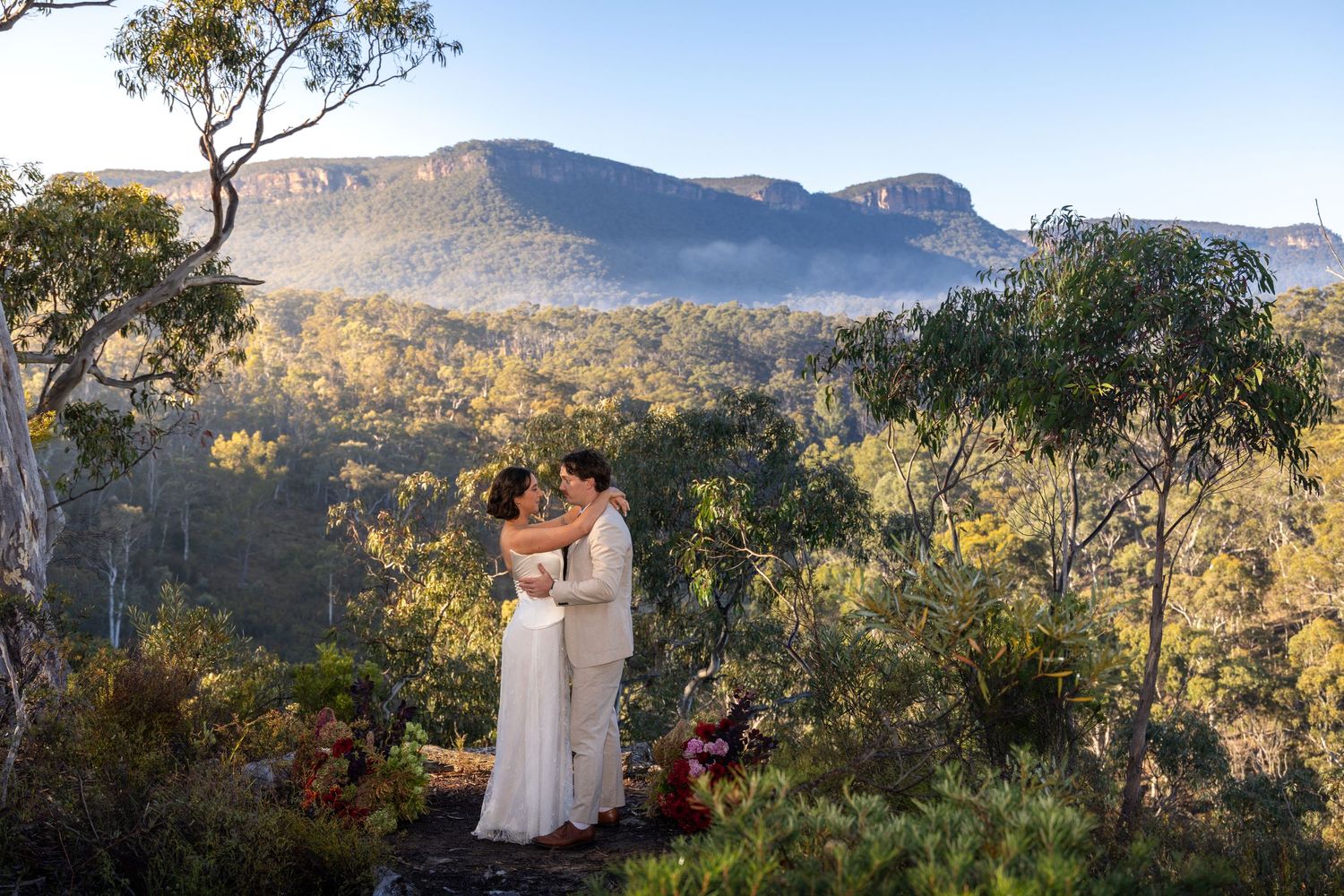 Bride and groom kissing on a rocky outcrop with stunning Blue Mountains forest and misty peaks in background at Maya Sanctuary.