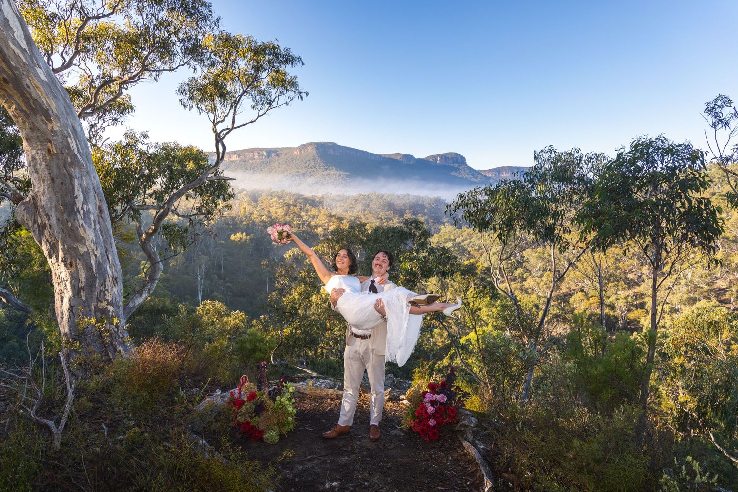 Couple celebrating outdoors in Australian bush landscape with misty mountains and eucalyptus trees in background at Maya Sanctuary.