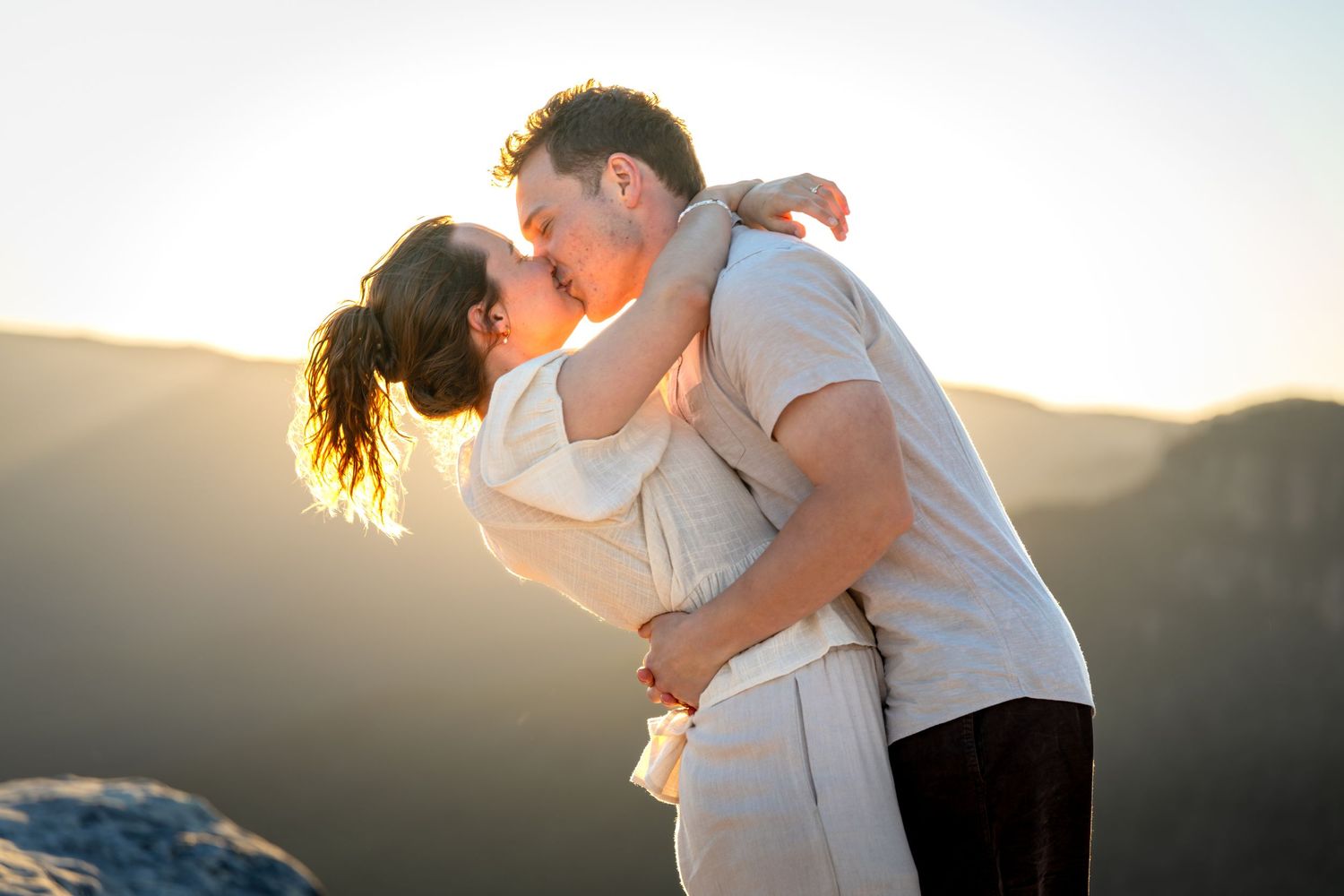 Romantic sunset engagement photo with couple embracing against mountain backdrop at Lincoln's Rock in Wentworth Falls, Blue Mountains.