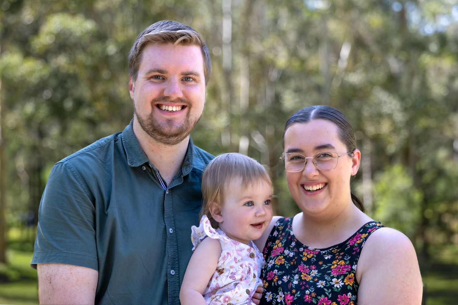 Family poses together outdoors in coordinated outfits among trees and greenery.