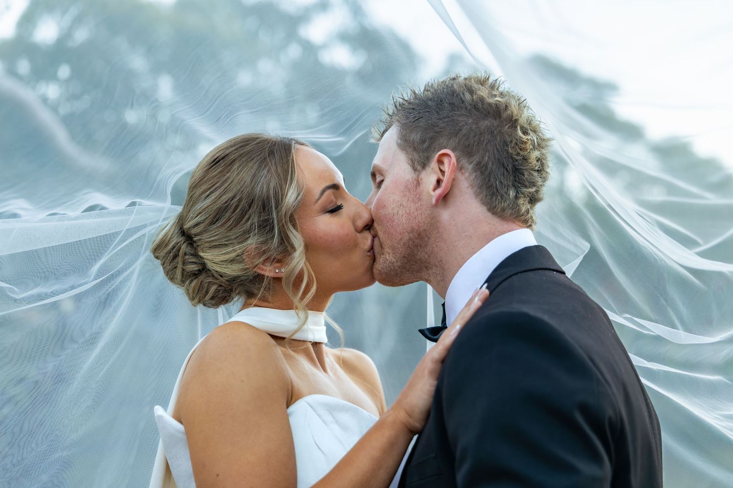 A bride and groom share a romantic kiss under a flowing white veil on their wedding day at Lawson Park, Hartley Vale.