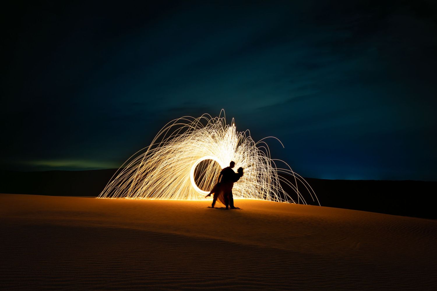 Spinning glowing steel wool on golden Stockton Sand Dunes at night, creating stunning couples photo.
