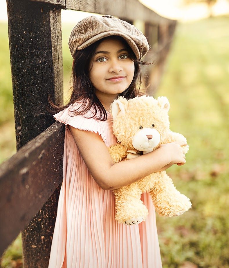 Child in pink dress holding teddy bear during outdoor portrait session.