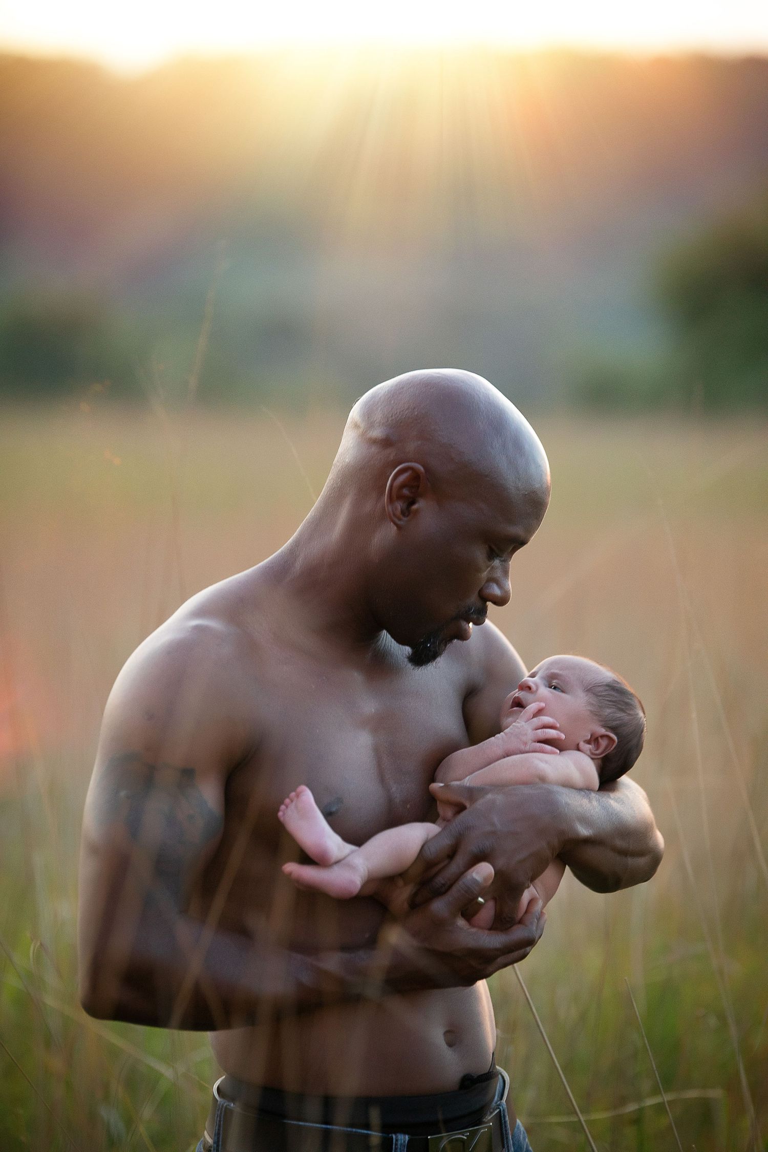 Parent and baby share intimate moments during outdoor sunset photoshoot.