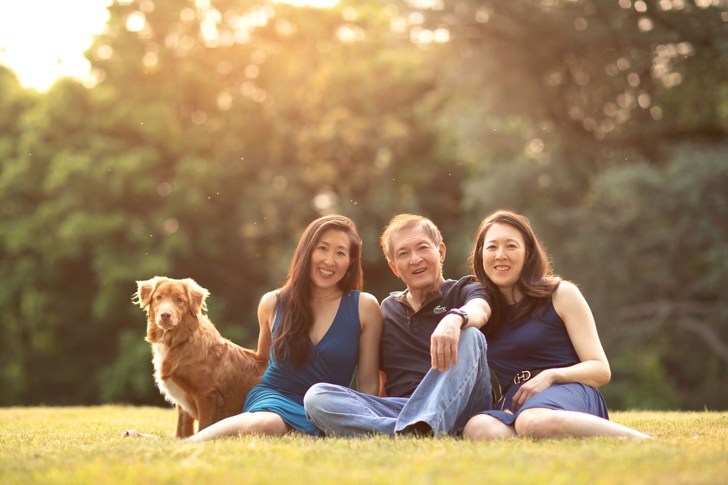 Group relaxing outdoors on grass with their golden retriever during sunset.