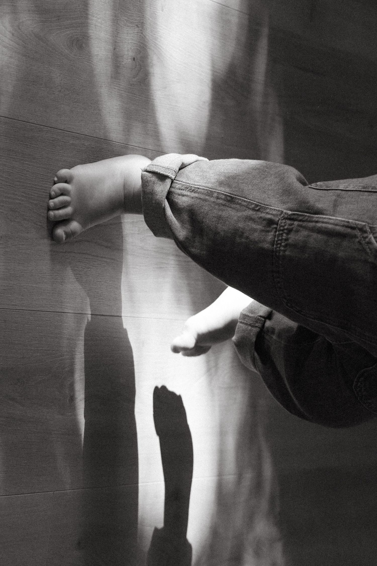Artistic black and white photograph of feet against window light creating shadows.