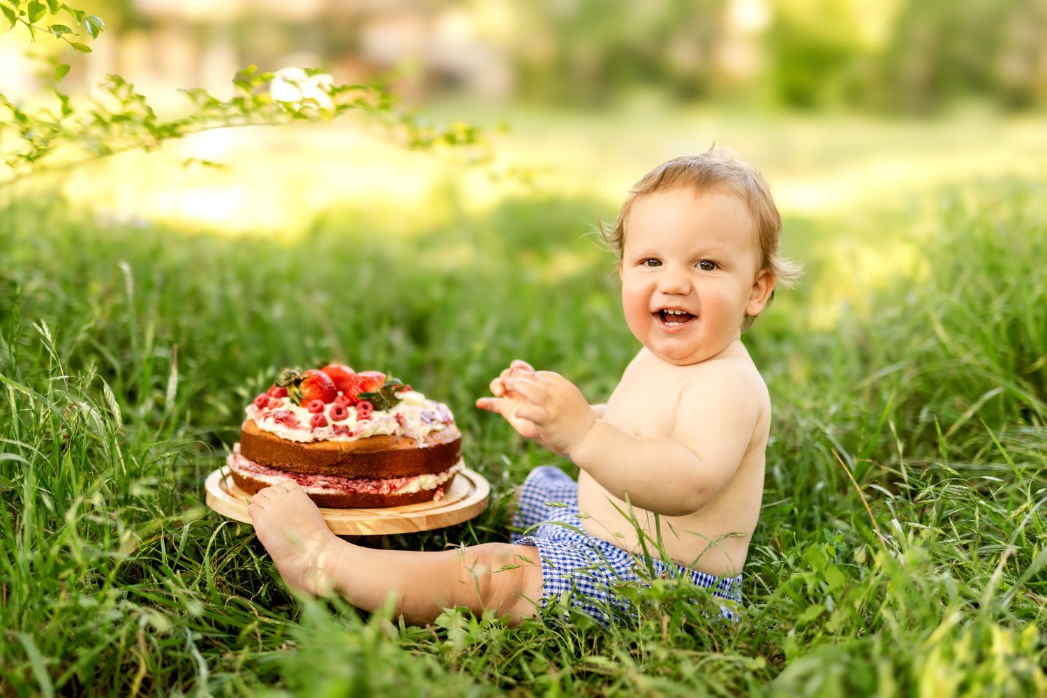 A baby sits in grass with a decorated chocolate cake.