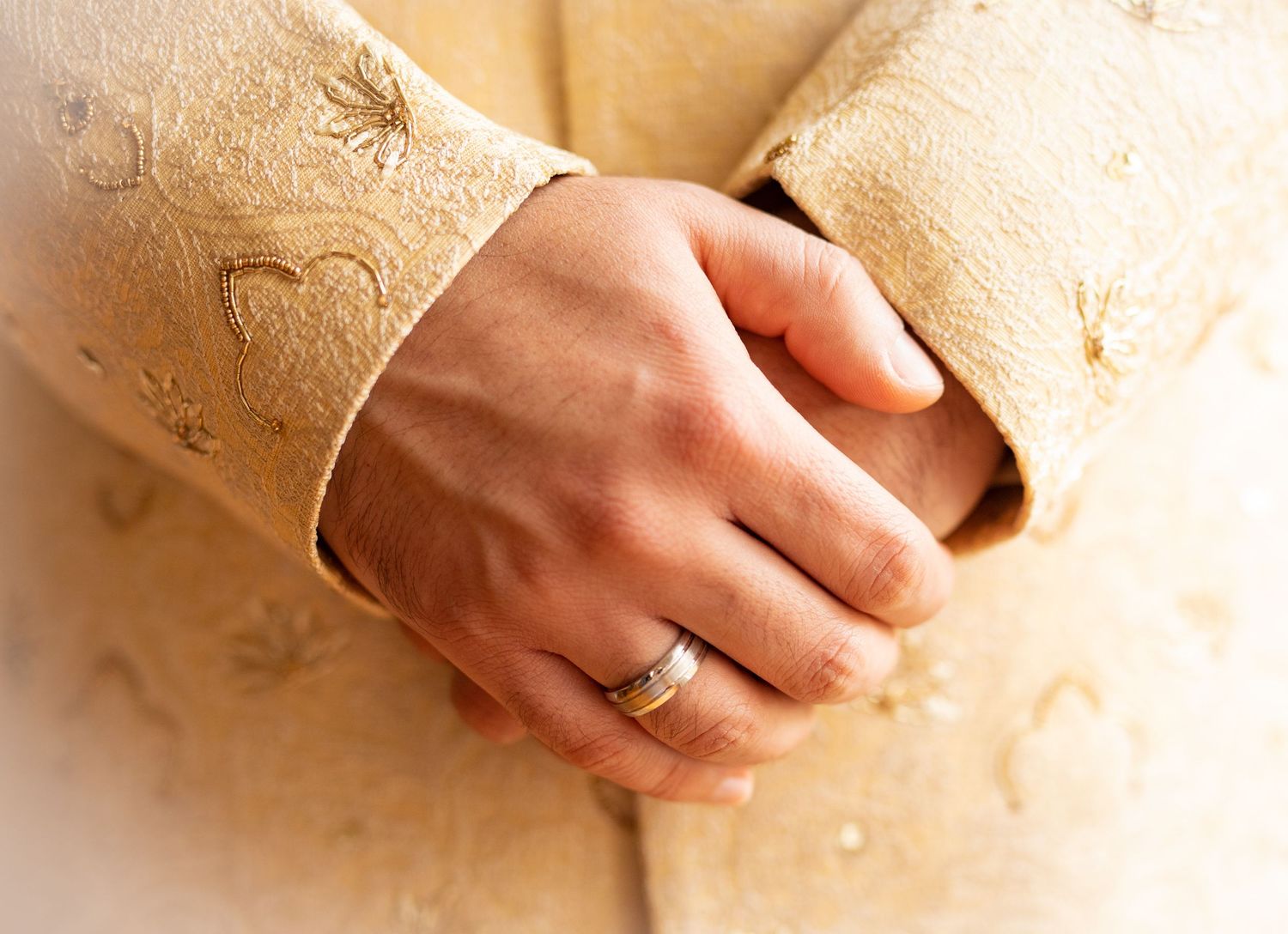 Close-up shot of hands with engagement ring against textured beige background.