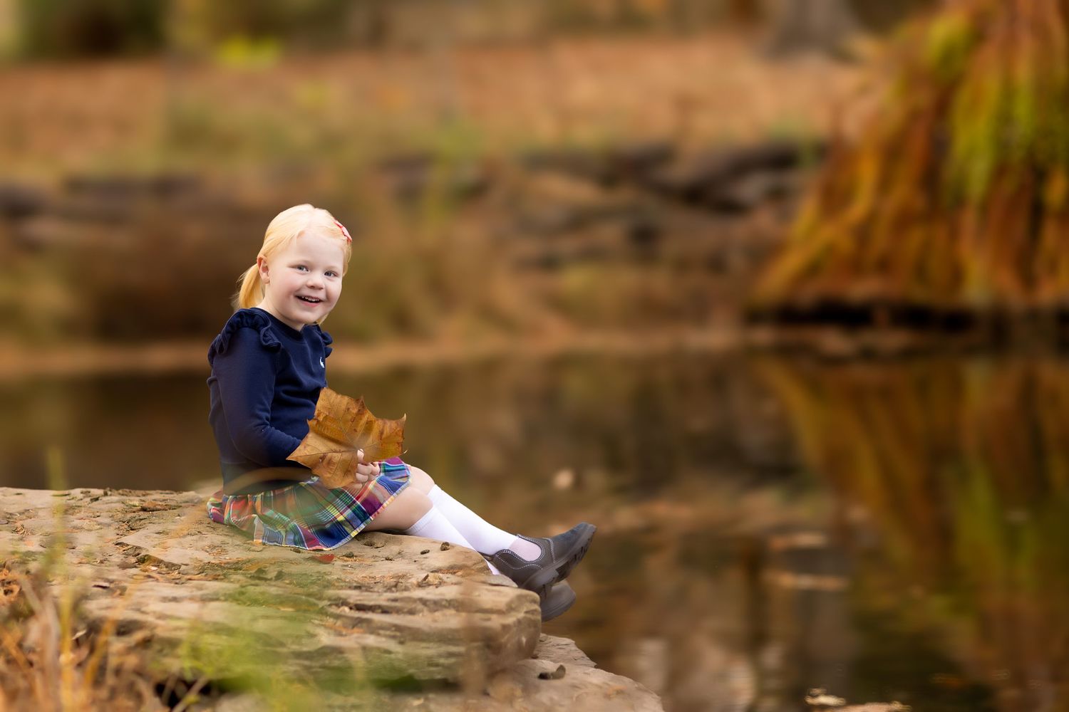 Children playing by a pond surrounded by fall foliage.
